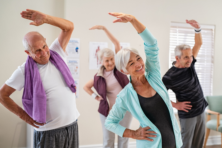 Group of seniors doing stretching exercise together at retirement centre. Elderly men and old women exercising at nursing home during daily fitness. Retired couples exercising at care facility.