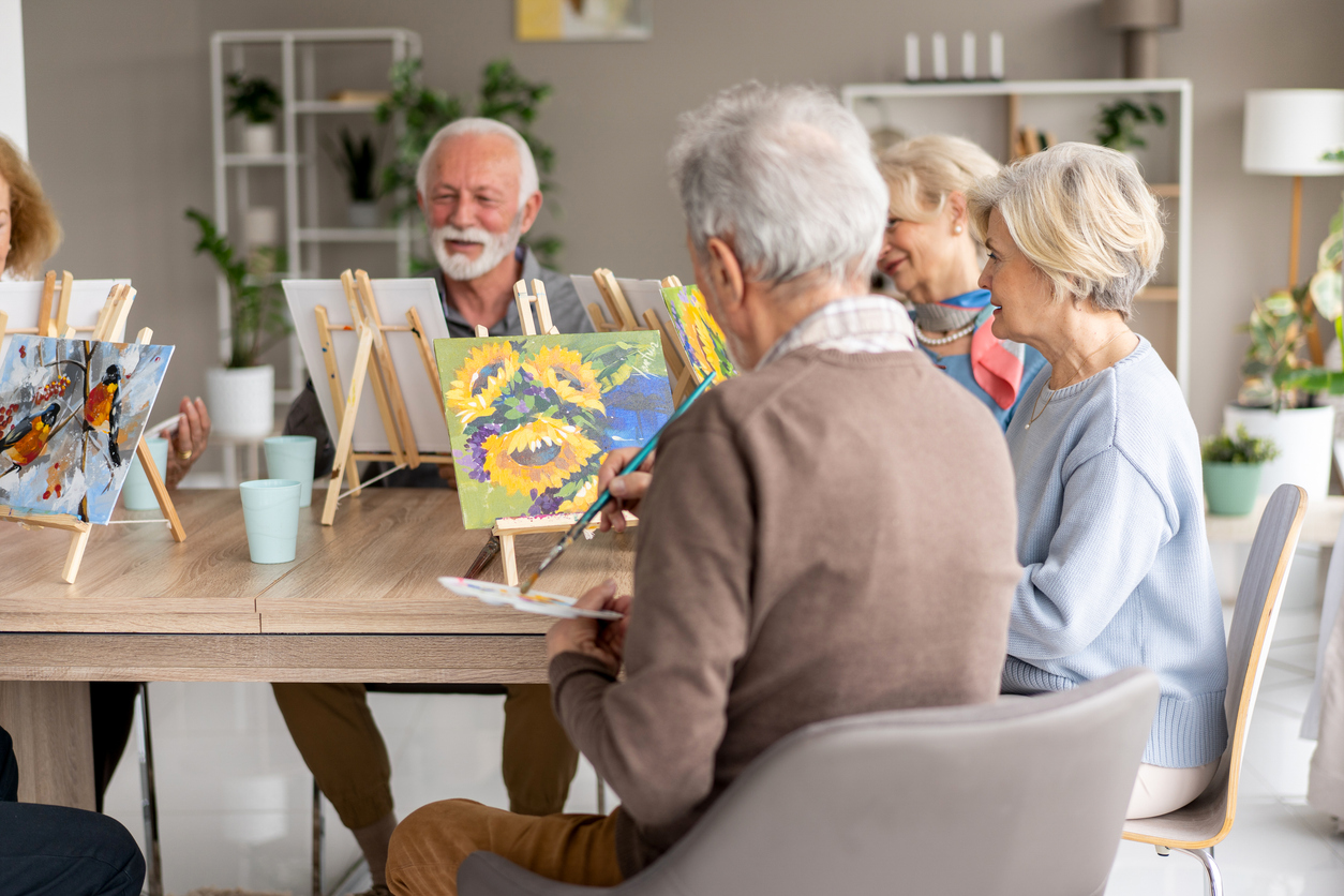 Elderly individuals participating in a painting class, showcasing creativity and interaction while creating beautiful artworks in a bright, welcoming room.