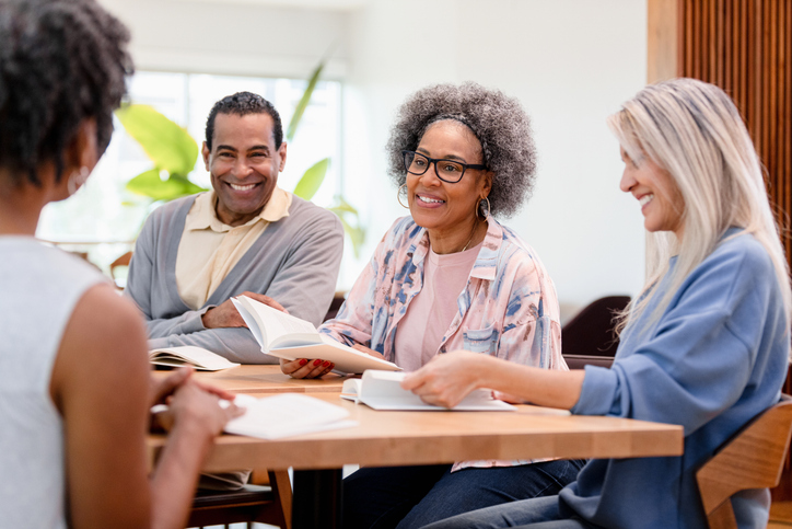 Smiling adults of different ethnicities participate in a book club meeting, showing togetherness and enjoyment.